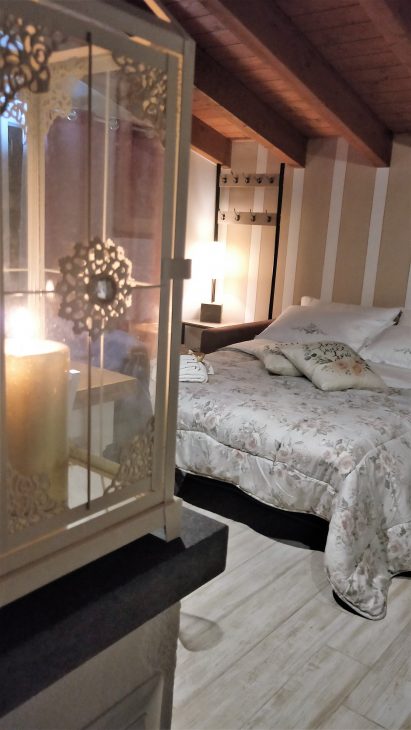 Sullo sfondo un letto ben rifatto in primo piano una candela accesa in una lanterna per un atmosfera romantica in Agriturismo