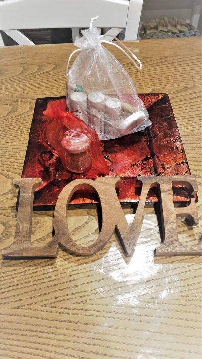 Kit di benvenuto in Agriturismo con bottigliette di sapone da bagno, scritta in legno Love, vasetto di origano su un vassoio rosso